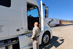 Law enforcement officer inspecting commercial truck cab at roadside checkpoint under clear sky