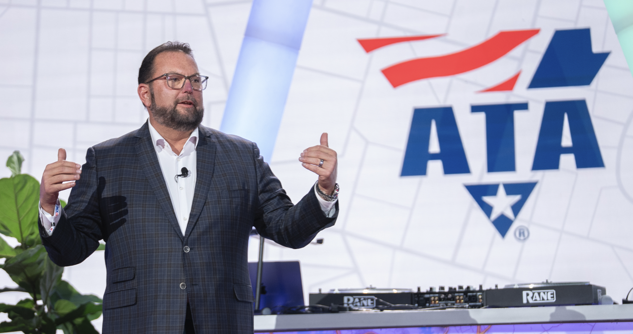 Professional speaker presenting at ATA conference with audio equipment and branded backdrop
