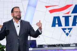 Professional speaker presenting at ATA conference with audio equipment and branded backdrop