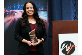 Woman in black blazer holding award at WT organization event with cityscape backdrop