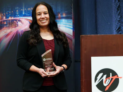 Woman in black blazer holding award at WT organization event with cityscape backdrop