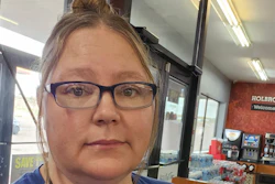 Woman wearing blue-framed glasses in a casual indoor setting with storefront signage visible in the background