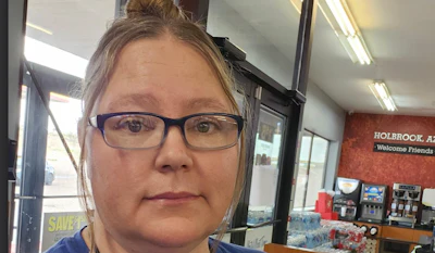 Woman wearing blue-framed glasses in a casual indoor setting with storefront signage visible in the background