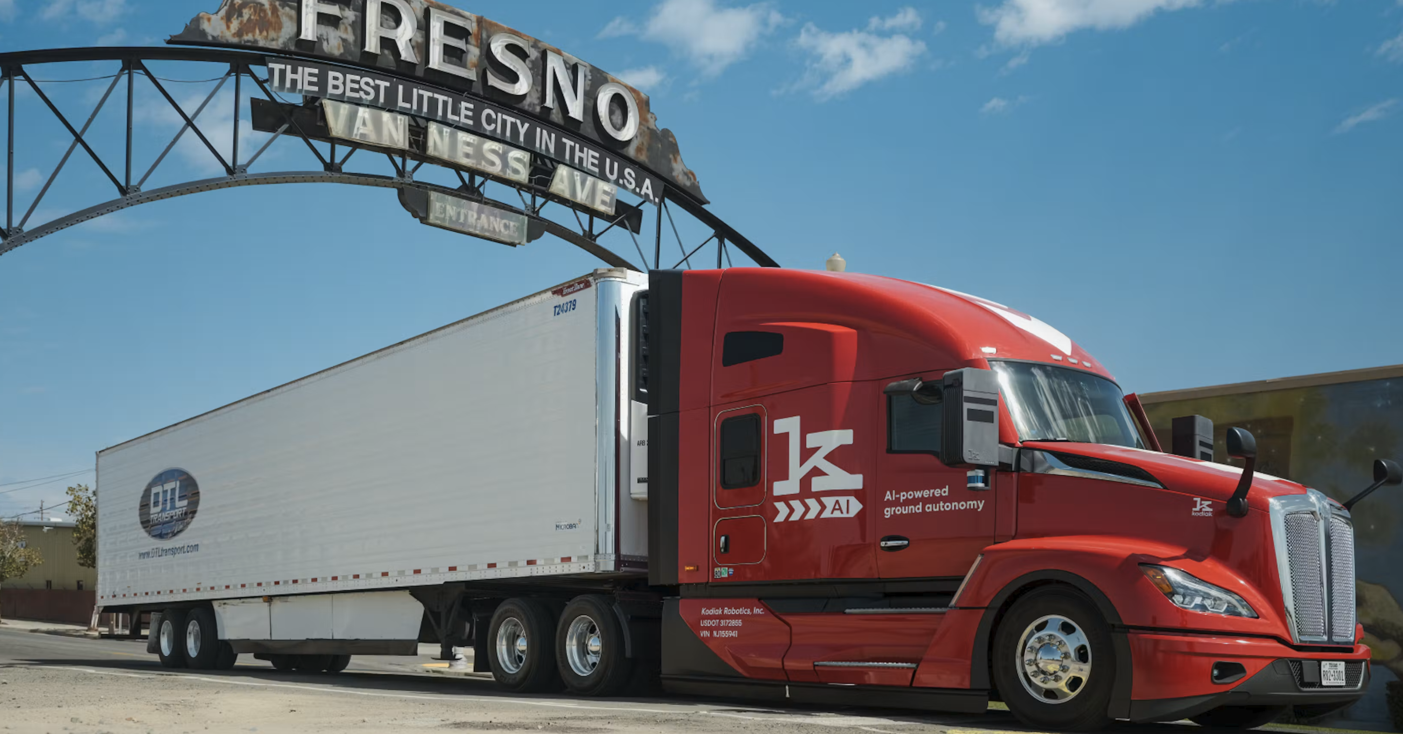 Red semi-truck with white refrigerated trailer under Fresno city sign in California