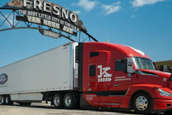 Red semi-truck with white refrigerated trailer under Fresno city sign in California