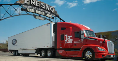 Red semi-truck with white refrigerated trailer under Fresno city sign in California