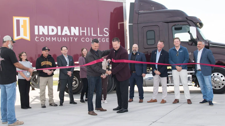 Group of officials and community members participate in ribbon-cutting ceremony at Indian Hills Community College event with branded vehicle